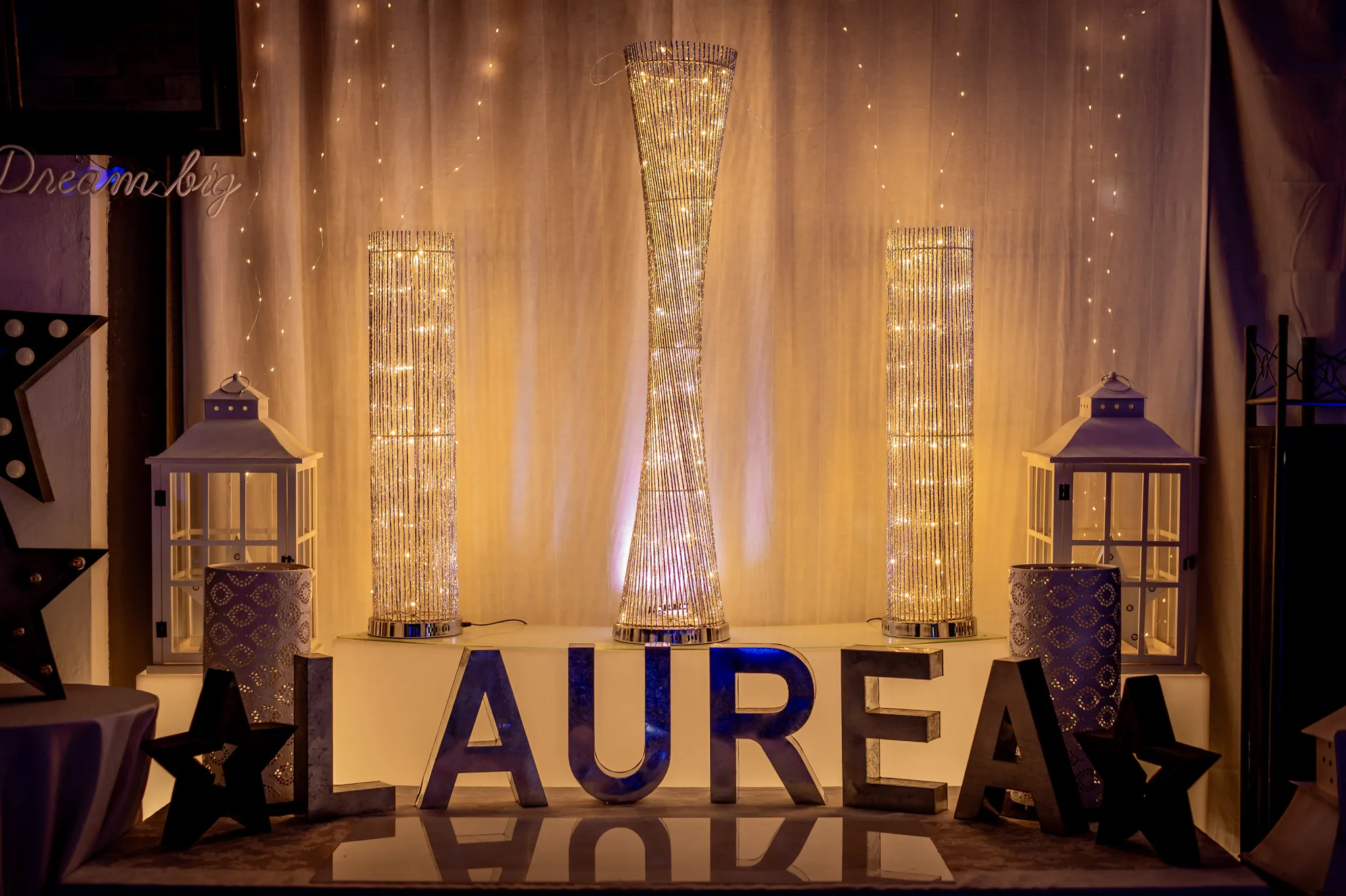 Scritta LAUREA a lettere luminose, affiancata da lanterne e colonne di luce: l’allestimento pronto per la festa